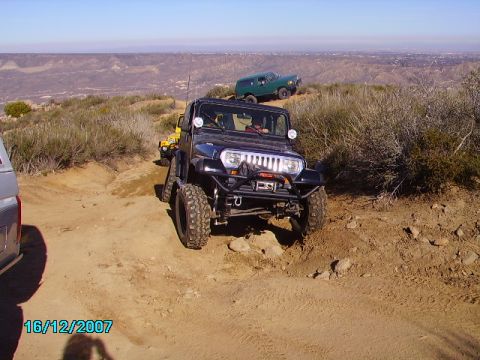 1990 Ford Bronco - Multiple off-road vehicles navigate a dusty trail with a panoramic view of the landscape below.