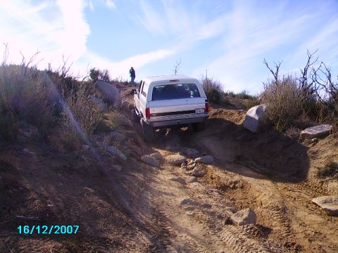 1990 Ford Bronco - A white 1990 Ford Bronco navigates a challenging rocky terrain on a sunny day.