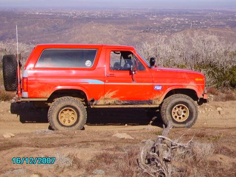 1990 Ford Bronco - This red Ford Bronco is parked on a dirt road overlooking a city.