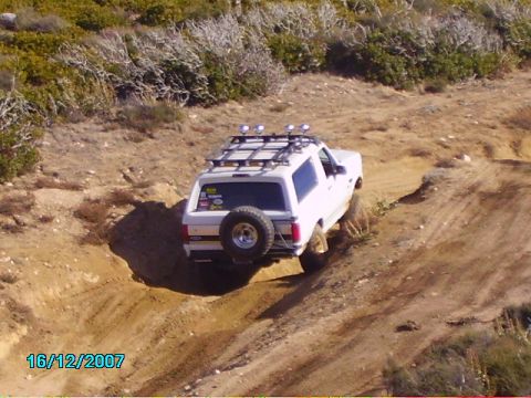 1990 Ford Bronco - A white SUV navigates a steep dirt path, its tires kicking up dust.