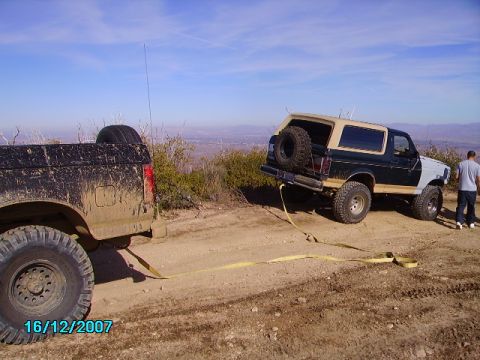 1990 Ford Bronco - A Ford Bronco and a Ford F-Series truck are stuck on a muddy hill, with a tow strap connecting them.