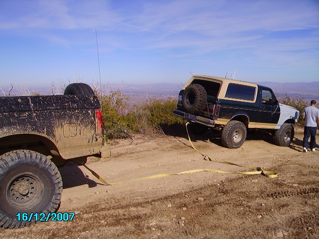 Two off-road vehicles stuck on a dirt hill, one being towed by the other