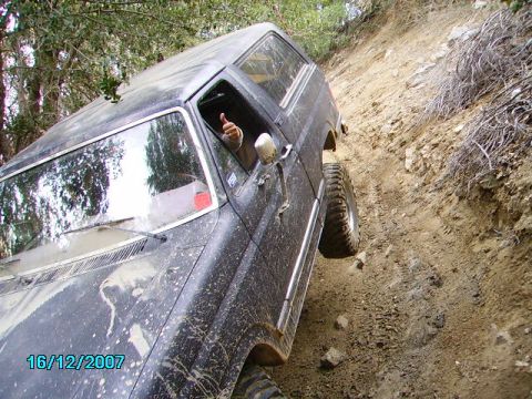 1990 Ford Bronco - A black 1990 Ford Bronco navigates a steep, muddy trail with a driver giving a thumbs-up from the window.