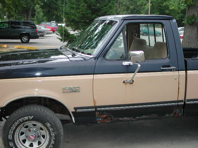 Side view of a two-tone blue and tan Ford F-Series pickup truck with rust on the lower body panels