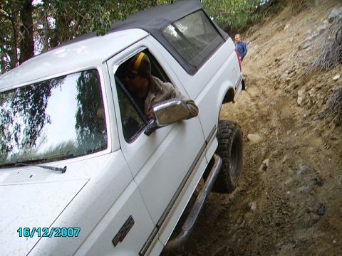1990 Ford Bronco - A white 1990 Ford Bronco navigates a steep, rocky dirt path with a person standing in the background.