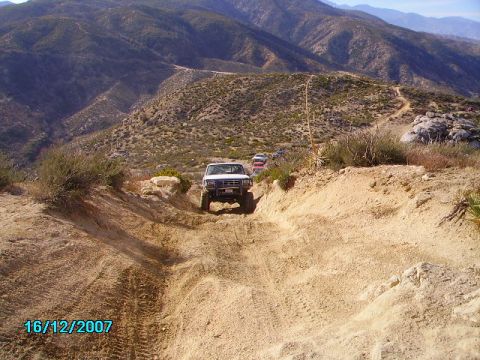 1990 Ford Bronco - White 1990 Ford Bronco navigates a challenging dirt trail in a mountainous landscape.