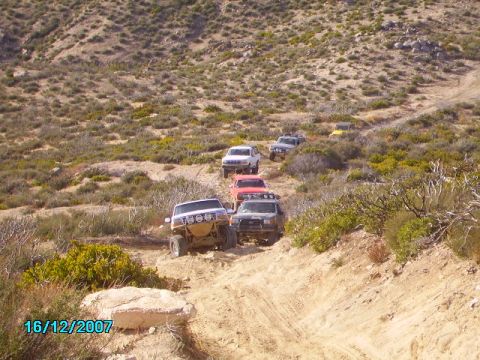 1990 Ford Bronco - A group of SUVs and trucks navigate a challenging off-road path through arid terrain.