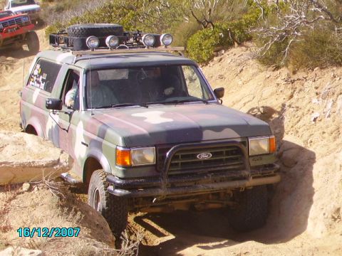 1990 Ford Bronco - A camouflaged Ford Bronco navigates a rocky, off-road trail with another vehicle visible in the background.