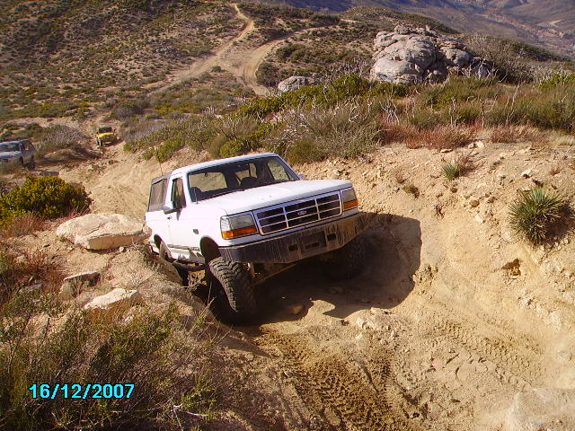White Ford Bronco navigating a rocky, off-road trail with another vehicle visible in the background