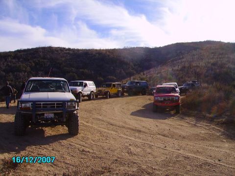 1990 Ford Bronco - Multiple SUVs, including a white Ford Bronco, are parked on a dusty trail in a hilly, arid landscape.