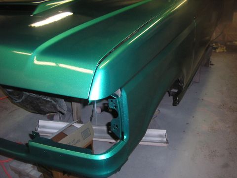 1987 Ford Bronco - The front section of a vehicle with a metallic green paint job is shown in a workshop setting.