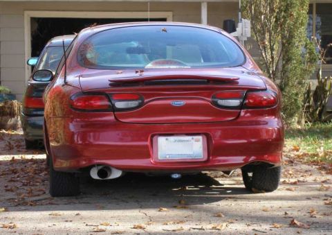 1997 Ford Taurus - The rear of a red sedan is shown, parked in front of a garage with another vehicle partially visible.