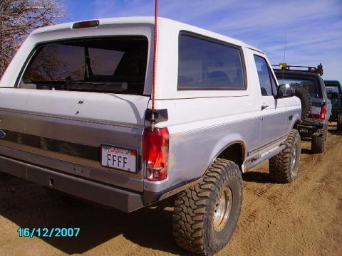 1990 Ford Bronco - A white and silver Ford Bronco is parked on a dirt road, with other vehicles behind it.