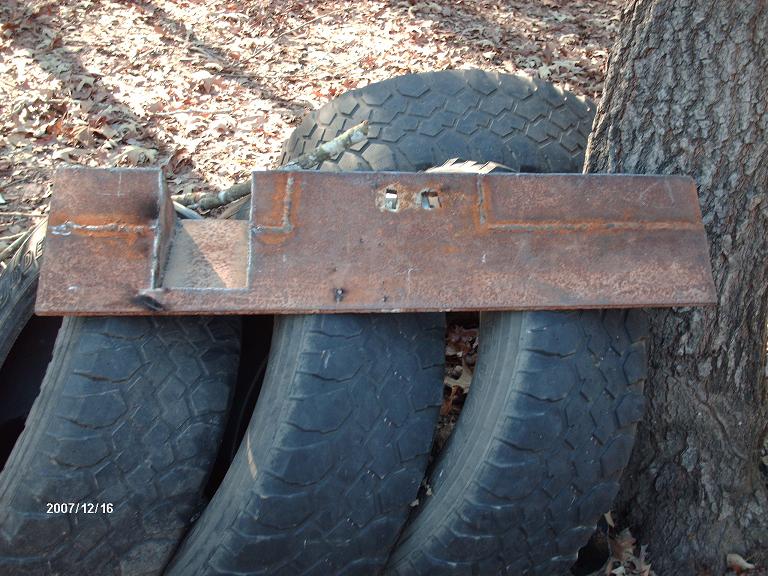 Fabricated steel bracket with two square cutouts, resting on stacked tires outdoors