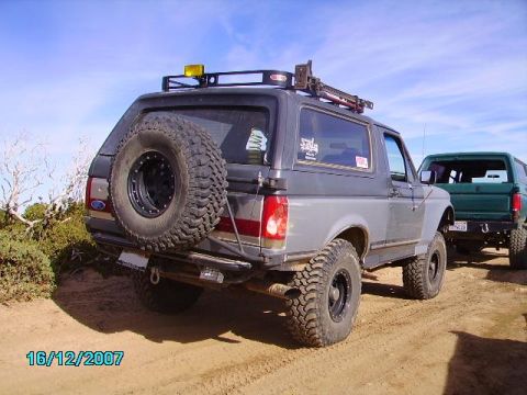 1990 Ford Bronco - Two SUVs are parked on a dirt road under a blue sky with scattered clouds.