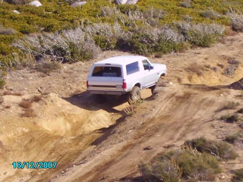 1990 Ford Bronco - This SUV is navigating a challenging dirt trail with steep inclines and loose terrain.
