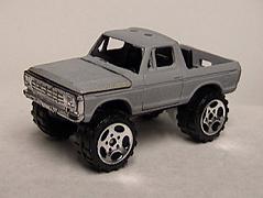 1979 Ford Bronco - A bare gray unpainted die-cast Ford Bronco/pickup body shown in a three-quarter front view, sitting on oversized knobby off-road tires with…