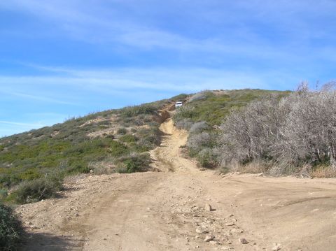 1985 Ford Bronco - Off-road vehicle ascends a challenging dirt track on a sunny day.