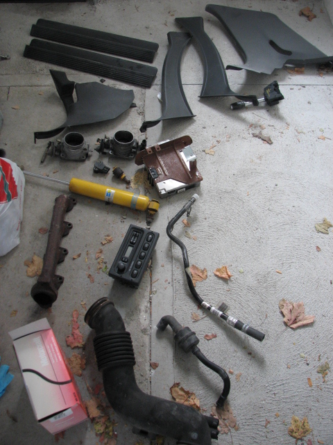 2003 Ford Crown Victoria - A collection of automotive parts, including engine components and interior trim, are displayed on a concrete floor.