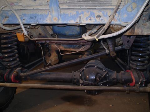 1986 Ford Bronco - The underside of a vehicle shows its drivetrain components and suspension system.