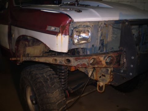 1986 Ford Bronco - The front end of a red and white truck shows off-road modifications and exposed engine components, with a prominent off-road tire visible.