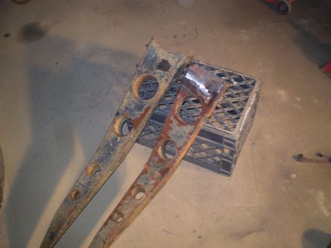 1986 Ford Bronco - Two rusty metal parts with multiple holes are resting on a crate in a garage.