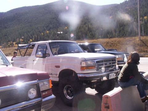 1986 Ford Bronco - A white Ford Bronco is parked outdoors with a mountainous backdrop and other vehicles nearby.