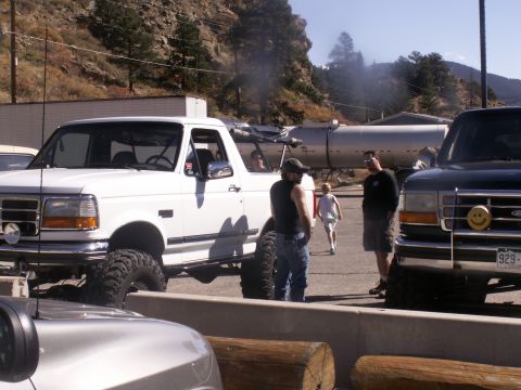 1986 Ford Bronco - A lifted white Ford Bronco is parked next to another truck, with people standing around.