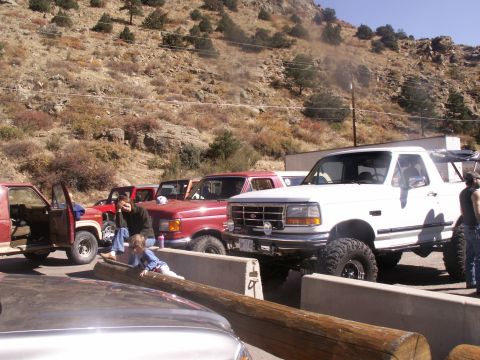 1986 Ford Bronco - Several trucks are parked in a dusty, rocky area with a hillside in the background.