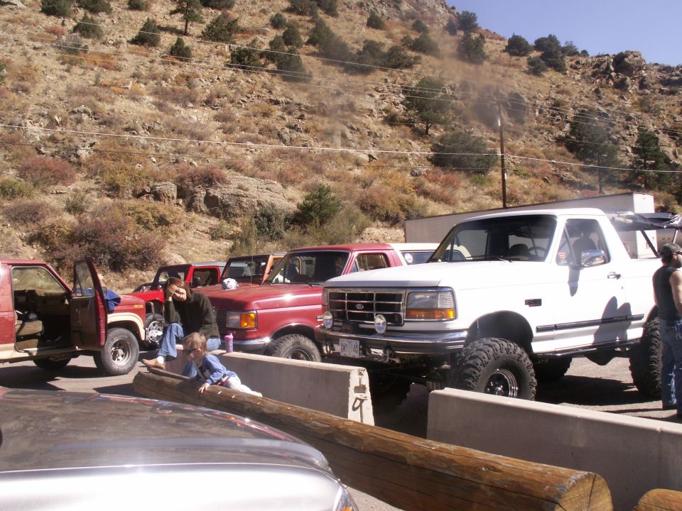 White Ford Bronco parked next to red trucks on a dirt road