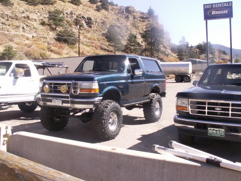 1986 Ford Bronco - This lifted Ford Bronco, likely from the early 1990s, is parked outdoors next to another Ford truck.