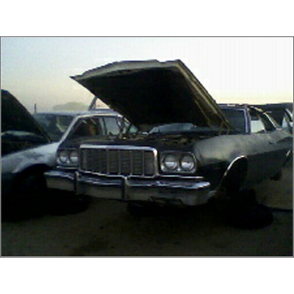 1973 Ford Ranchero front end with hood open, parked in junkyard next to another car