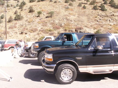 1986 Ford Bronco - Several Ford Broncos are parked in a line on a dusty lot with a hillside in the background.