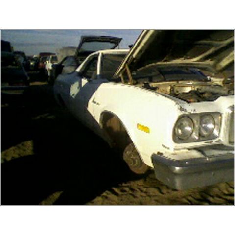 1973 Ford Ranchero - A white pickup truck sits in a junkyard, its hood open, surrounded by other vehicles under a cloudy sky.