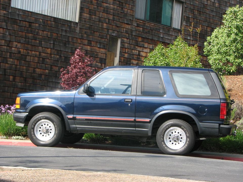 Blue two-door SUV parked on a street, side view. Building in background