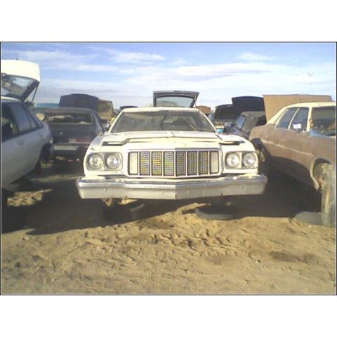 1973 Ford Ranchero - A white 1972 Ford Gran Torino sits in a junkyard, its front end elevated on tires, with other vehicles visible in the background.