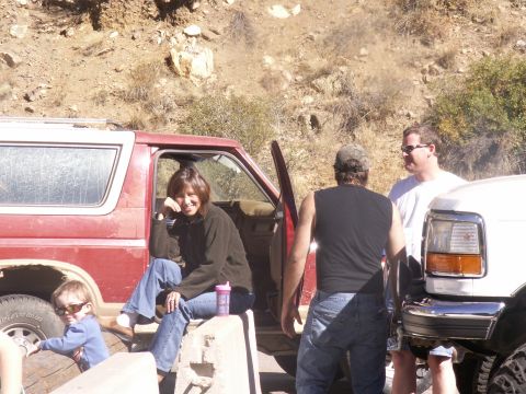 1986 Ford Bronco - A group of people are gathered around a red 1986 Ford Bronco, with another white vehicle partially visible.