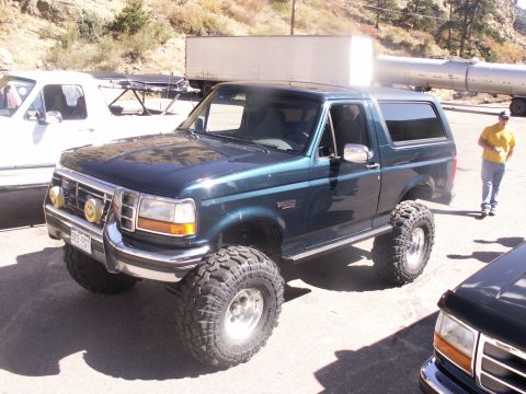 1986 Ford Bronco - This lifted Ford Bronco is parked outdoors with other vehicles and a trailer in the background.