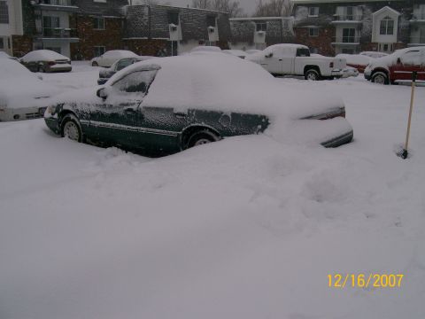 1995 Mercury Grand Marquis - A dark green sedan is almost completely covered by snow, with only a portion of its side visible.