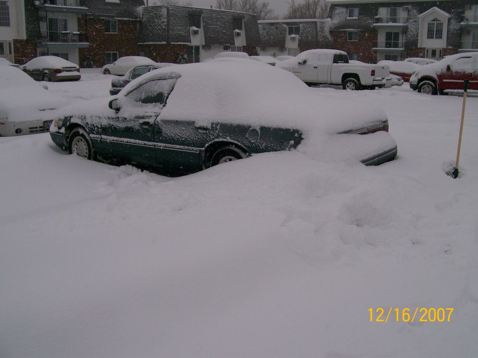 Side view of a dark green sedan buried in snow