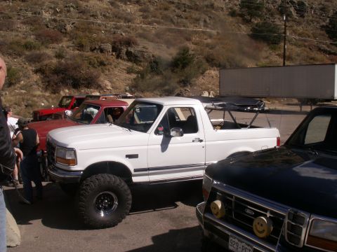 1986 Ford Bronco - White Ford Bronco with off-road tires is parked in a lot with other vehicles.
