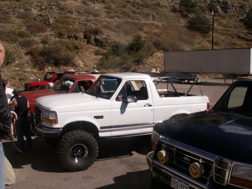 White Ford Bronco with large off-road tires parked next to other vehicles