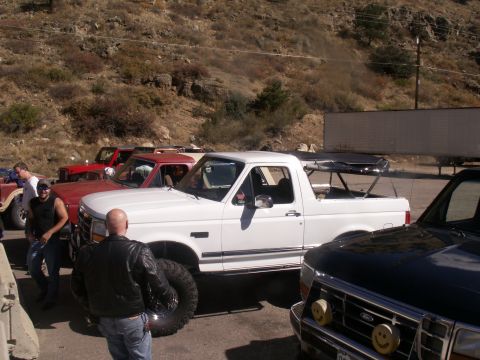 1986 Ford Bronco - Several off-road vehicles are gathered on a dusty roadside with a rocky hillside in the background.