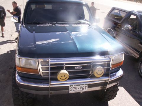 1986 Ford Bronco - This dark green Ford truck, likely from the early to mid-1990s, is parked next to another vehicle.