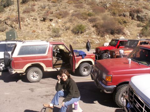 1986 Ford Bronco - A group of off-road vehicles are parked in a lot with a rocky hillside in the background.