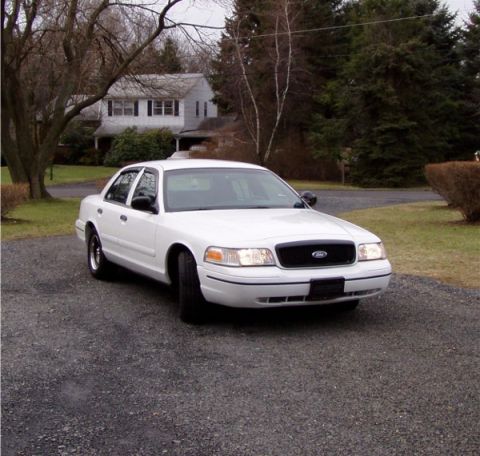 1999 Ford Crown Victoria - A white 1999 Ford Crown Victoria is parked on a gravel driveway in front of a house.