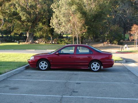1992 Ford Taurus - A red sedan is parked in a lot with trees in the background. The vehicle appears to be a 1998 Ford Contour.