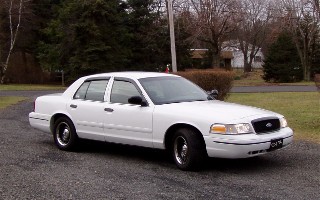1999 Ford Crown Victoria - This white 1999 Ford Crown Victoria is parked outside on a gravel driveway with trees in the background.