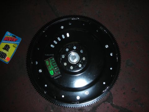 1992 Ford Crown Victoria - A black flywheel with a toothed outer edge and a package of ARP bolts are shown.