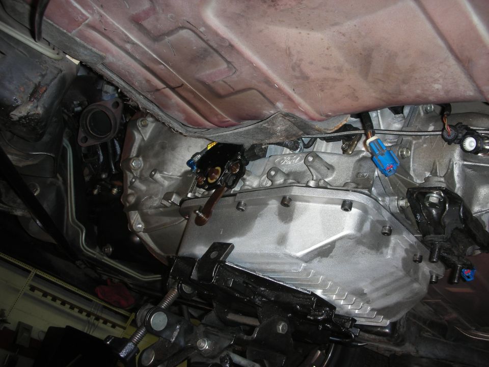 Underside view of a vehicle's transmission and exhaust pipe, supported by a jack